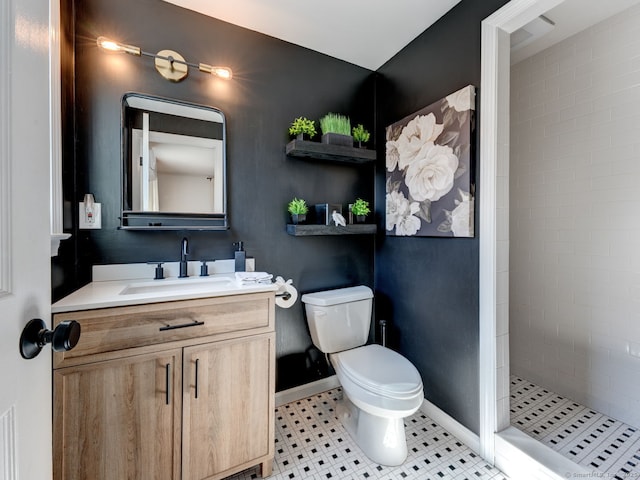 bathroom with baseboards, toilet, vanity, and a tile shower