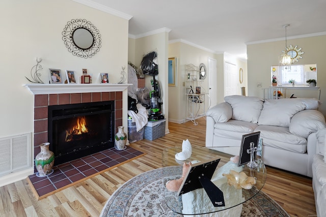 living room with visible vents, wood finished floors, a tiled fireplace, and crown molding