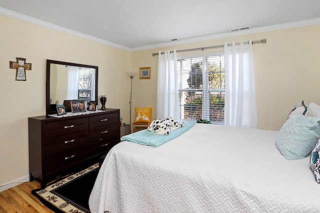 bedroom with visible vents, crown molding, and light wood-style floors