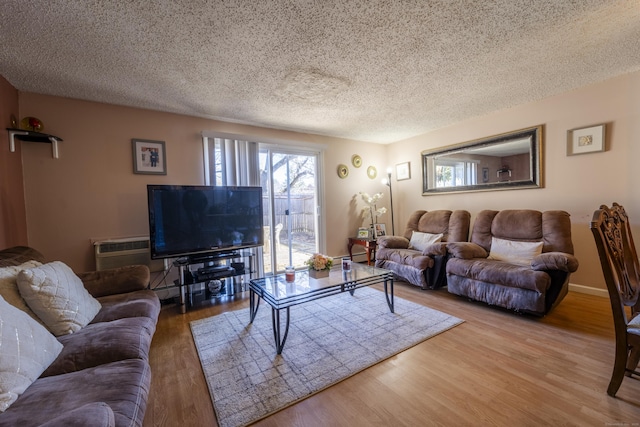 living area with baseboards, a textured ceiling, a wall unit AC, and wood finished floors