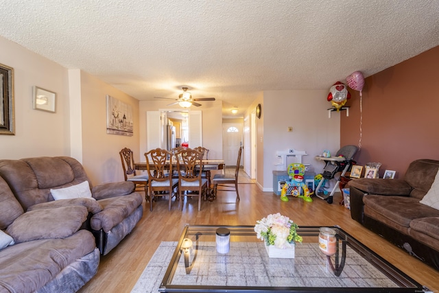 living area featuring light wood-style flooring, a textured ceiling, and a ceiling fan