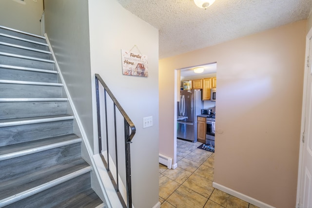 staircase featuring a baseboard heating unit, baseboards, tile patterned flooring, and a textured ceiling