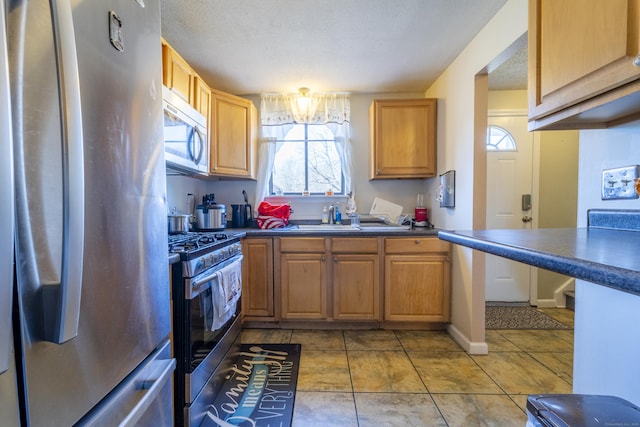 kitchen featuring light tile patterned floors, a sink, stainless steel appliances, a textured ceiling, and dark countertops