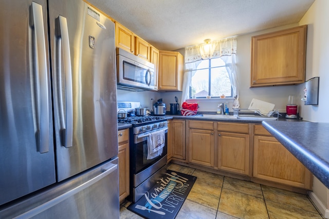 kitchen featuring a textured ceiling, dark countertops, a sink, and stainless steel appliances