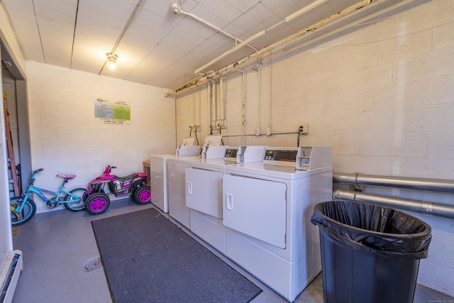 common laundry area featuring washing machine and clothes dryer, baseboard heating, and concrete block wall