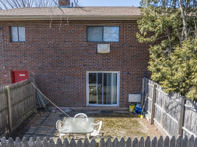 back of property featuring a fenced backyard, a shingled roof, a chimney, a patio area, and brick siding