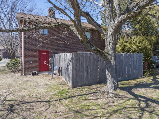 view of front of house featuring brick siding, a chimney, and fence