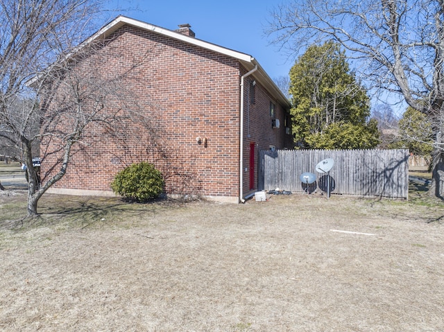 view of side of home featuring fence, brick siding, and a chimney