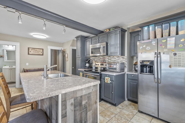 kitchen with a breakfast bar, a sink, appliances with stainless steel finishes, a toaster, and decorative backsplash