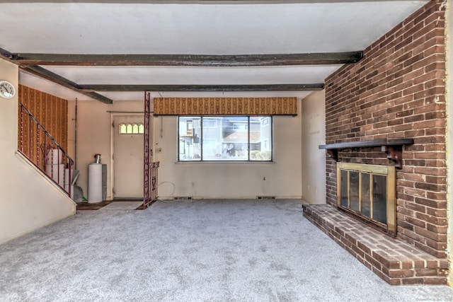 unfurnished living room featuring beamed ceiling, carpet, a brick fireplace, and visible vents