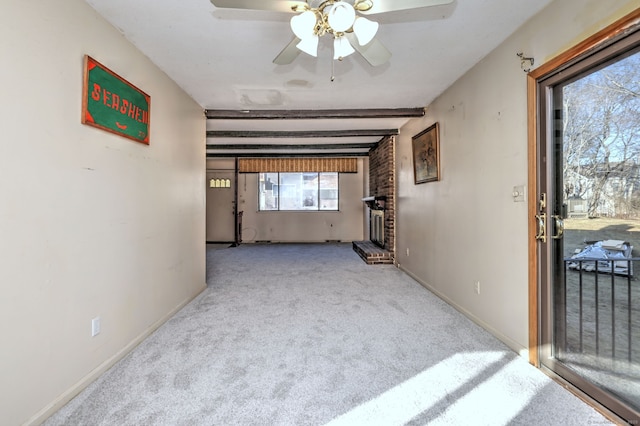 spare room featuring a ceiling fan, baseboards, beam ceiling, a brick fireplace, and carpet flooring