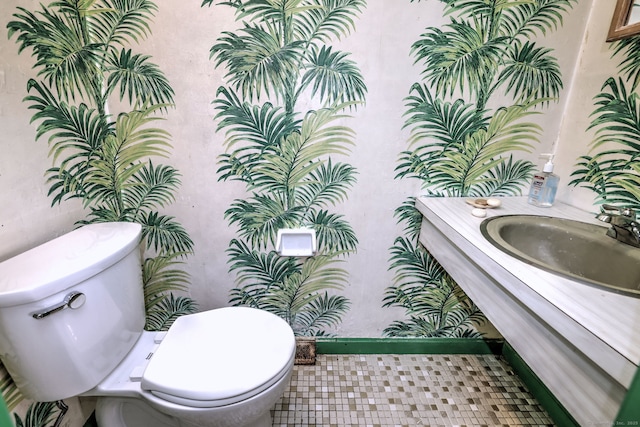 half bath with wallpapered walls, toilet, vanity, and baseboards