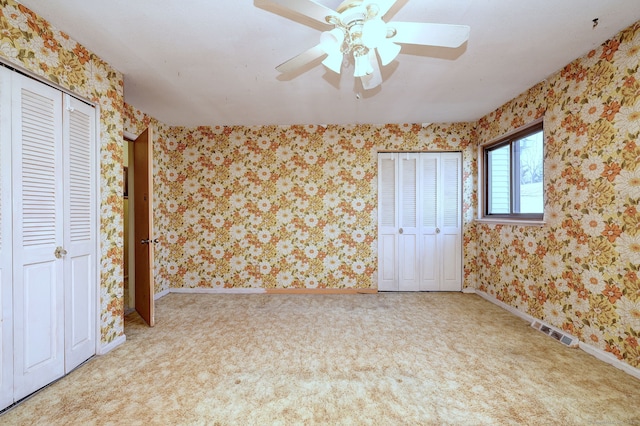 unfurnished bedroom with baseboards, visible vents, carpet floors, wallpapered walls, and two closets