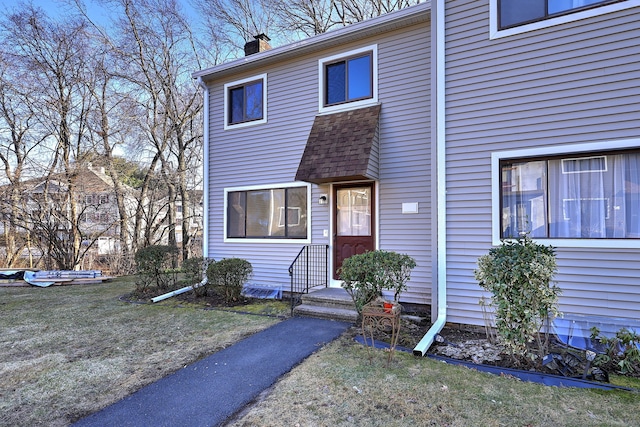 view of front of property featuring a shingled roof, a front lawn, and a chimney