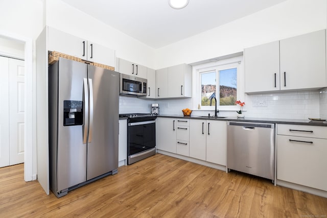 kitchen featuring a sink, light wood-style floors, dark countertops, and appliances with stainless steel finishes