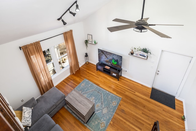 living room with baseboards, ceiling fan, rail lighting, wood finished floors, and high vaulted ceiling