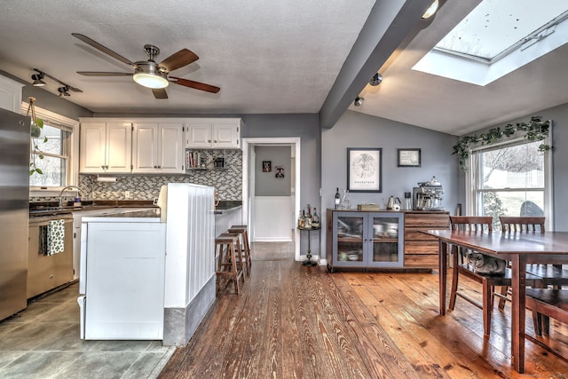 kitchen with wood finished floors, ceiling fan, lofted ceiling with skylight, dishwasher, and dark countertops