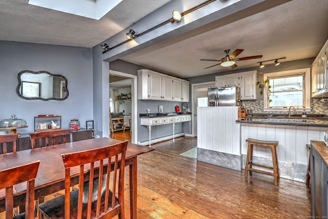 dining room with a textured ceiling, wood finished floors, a baseboard heating unit, and ceiling fan