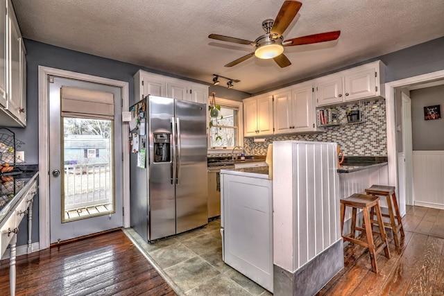 kitchen featuring stainless steel fridge with ice dispenser, ceiling fan, hardwood / wood-style flooring, white cabinetry, and dark countertops