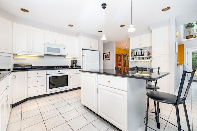 kitchen with a breakfast bar, white appliances, light tile patterned floors, and white cabinetry