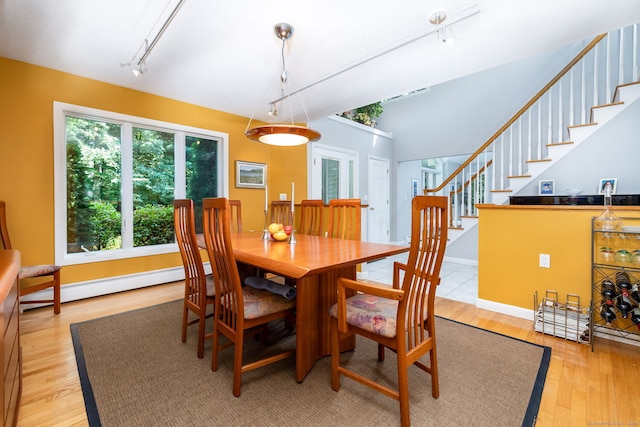 dining room with stairway, baseboards, rail lighting, light wood-style floors, and baseboard heating