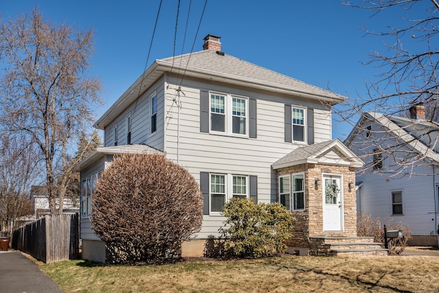 view of front of property featuring a chimney, stone siding, a shingled roof, and fence