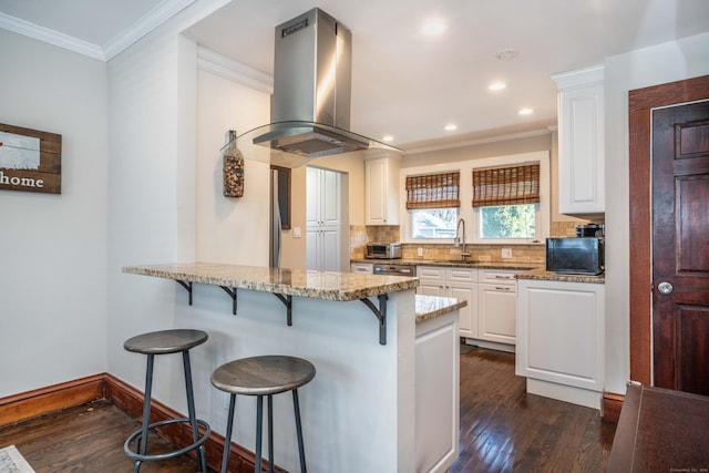 kitchen featuring light stone countertops, a kitchen breakfast bar, island range hood, white cabinetry, and a sink