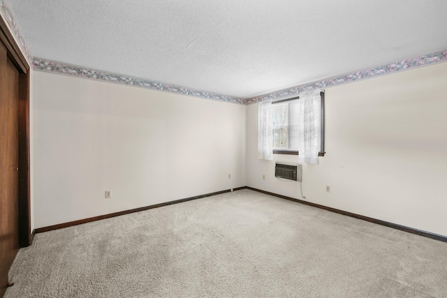 unfurnished bedroom featuring a wall mounted air conditioner, baseboards, carpet floors, and a textured ceiling