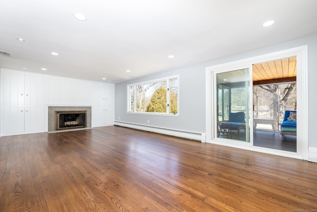 unfurnished living room featuring wood finished floors, a wealth of natural light, and a baseboard radiator