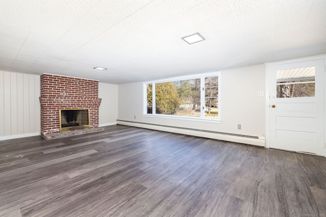 unfurnished living room with a textured ceiling, wood finished floors, baseboards, baseboard heating, and a brick fireplace