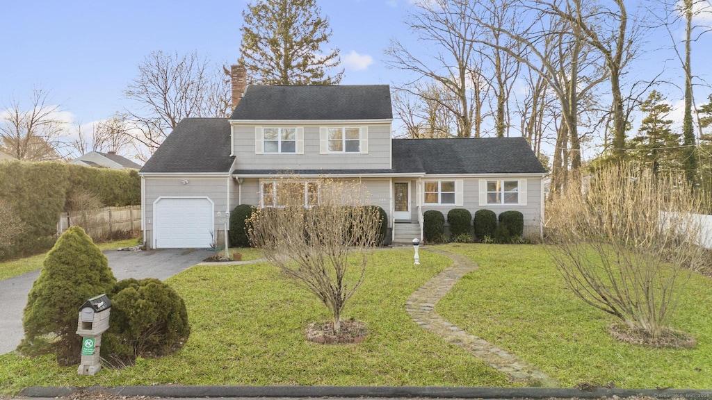 traditional-style home with driveway, a front yard, a chimney, and an attached garage