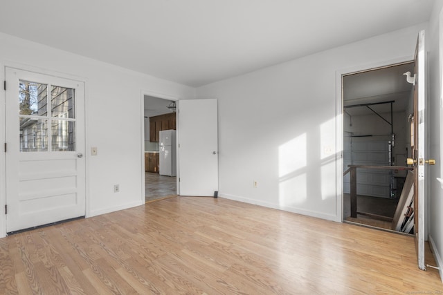 unfurnished bedroom featuring baseboards, wood finished floors, and freestanding refrigerator