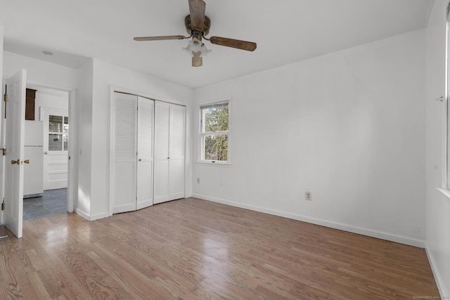 unfurnished bedroom with a ceiling fan, wood finished floors, baseboards, freestanding refrigerator, and a closet