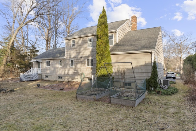 back of house with central AC unit, a chimney, a vegetable garden, and roof with shingles