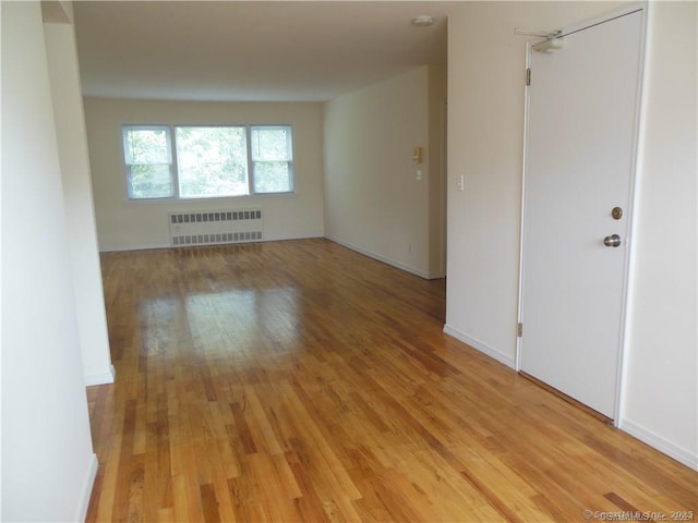 unfurnished room with light wood-style flooring, radiator heating unit, and baseboards