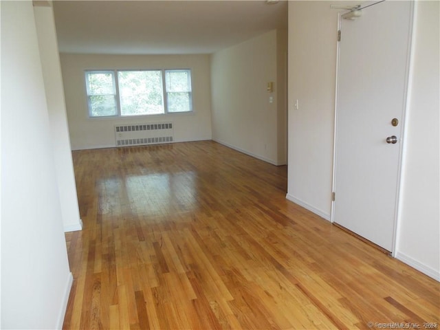 empty room featuring radiator heating unit, baseboards, and light wood-type flooring