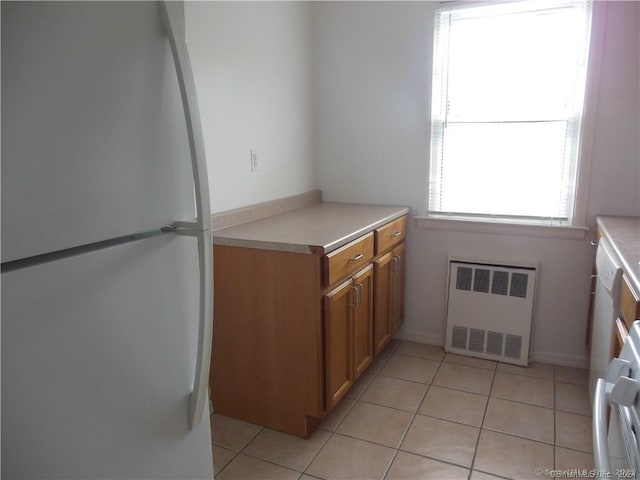 kitchen featuring freestanding refrigerator, radiator, light tile patterned flooring, brown cabinetry, and light countertops