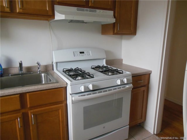 kitchen featuring under cabinet range hood, white range with gas stovetop, brown cabinetry, and a sink