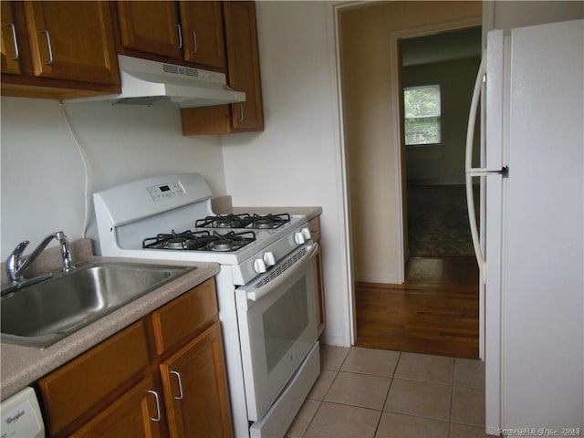 kitchen with white appliances, light tile patterned floors, a sink, light countertops, and under cabinet range hood