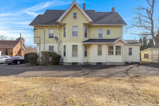 rear view of property featuring a shingled roof and a chimney