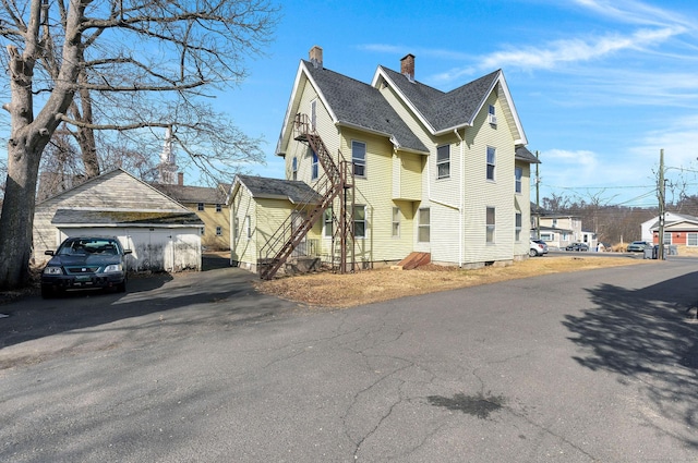 view of property exterior featuring an outdoor structure, a residential view, roof with shingles, and a chimney