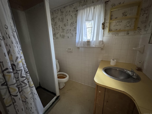 full bathroom featuring toilet, a stall shower, wainscoting, wallpapered walls, and vanity