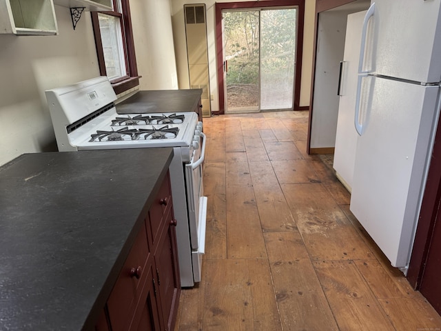 kitchen featuring dark countertops, white appliances, light wood-type flooring, and baseboards