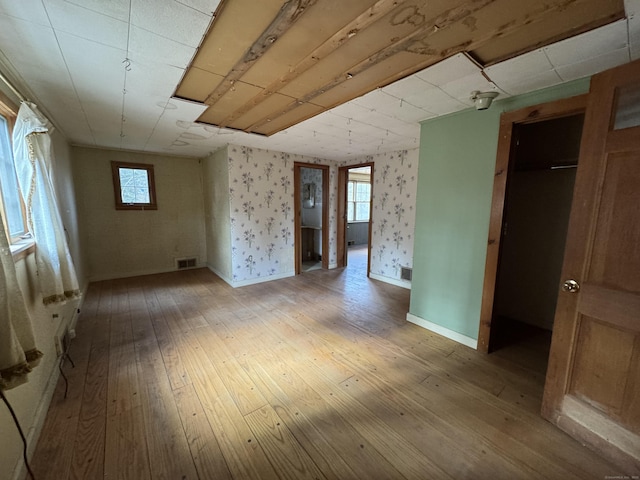 empty room featuring wallpapered walls, visible vents, light wood-type flooring, and baseboards