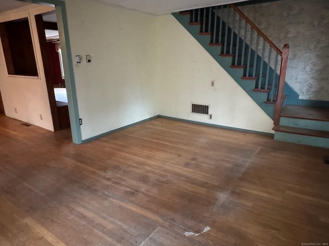 unfurnished living room with visible vents, stairway, and wood finished floors