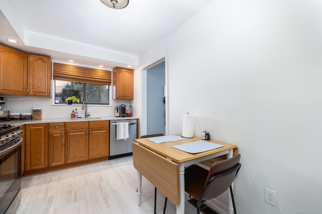 kitchen with brown cabinetry, a sink, gas range oven, and stainless steel dishwasher