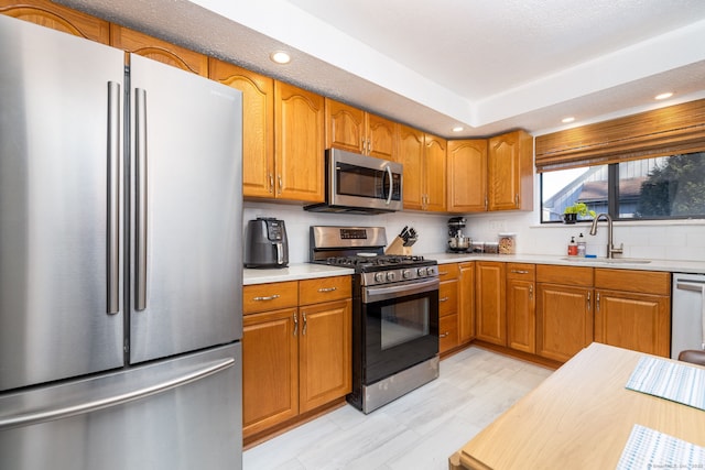 kitchen featuring brown cabinets, a sink, tasteful backsplash, appliances with stainless steel finishes, and light countertops