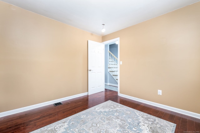 empty room with stairs, visible vents, baseboards, and dark wood-style flooring