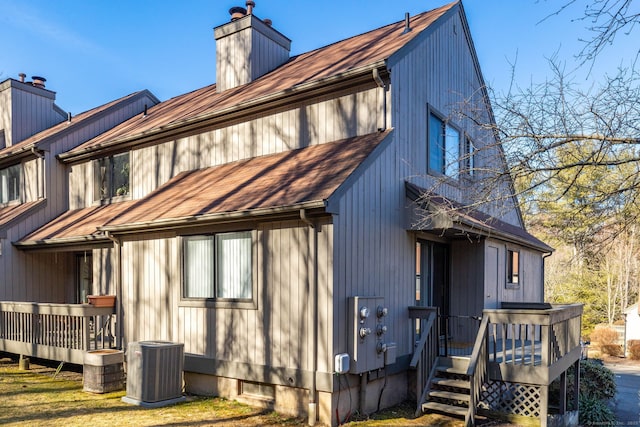 back of house with a wooden deck, a chimney, and central AC