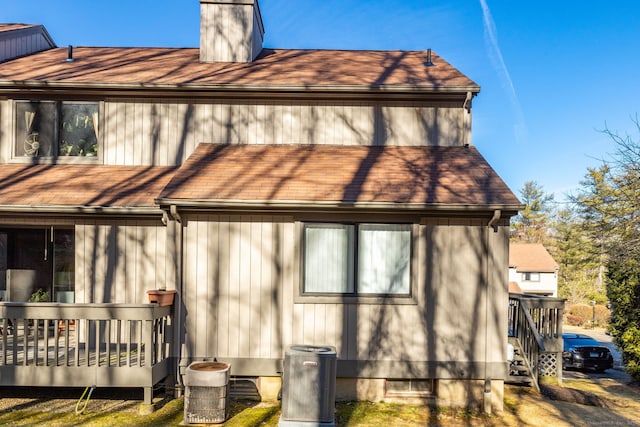 back of property with a wooden deck, central air condition unit, and a chimney